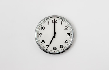 White Clock hanging on a white wall showing time 7:00
