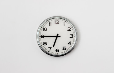 White Clock hanging on a white wall showing time 6:45