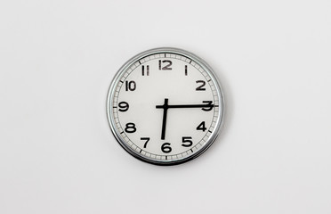 White Clock hanging on a white wall showing time 6:15