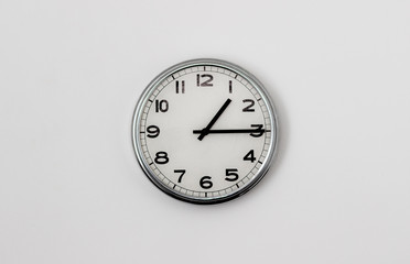 White Clock hanging on a white wall showing time 1:15
