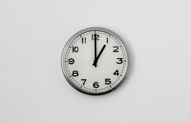 White Clock hanging on a white wall showing time 1:00