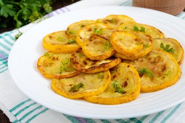 Fried zucchini slices on a white plate on a dark wooden background.