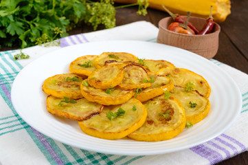 Fried zucchini slices on a white plate on a dark wooden background.