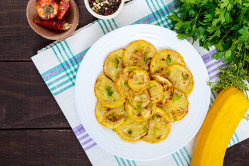 Fried zucchini slices on a white plate on a dark wooden background. Top view.