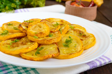 Fried zucchini slices on a white plate on a dark wooden background. Close up