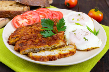 Pieces of chop (schnitzel), toast with eggs, fresh tomato on a dark wooden background.