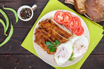 Pieces of chop (schnitzel), toast with eggs, fresh tomato on a dark wooden background. Top view.