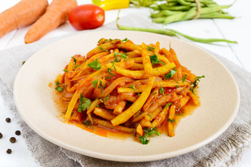 Spicy warm salad of green beans in tomato sauce on a plate on a white wooden background. Vegan dish.