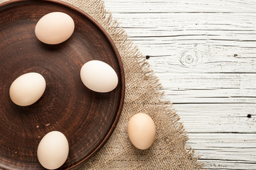 chicken eggs in clay plate on white wooden background