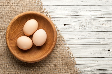 chicken eggs in wooden plate on white wooden background