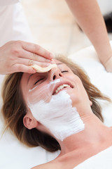 Beautiful woman with clear skin getting facial mask at salon
