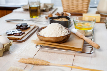 Baking ingredients in rural kitchen - dough recipe ingredients (eggs, flour, milk, butter, sugar) and rolling pin on wooden white table.