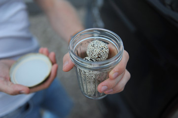 Energy sweets from dried fruits sprinkled with sesame seeds in a faceted glass in a man's hand