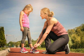 Mother and daughter outdoors. Mother tying laces on sneakers her daughter.