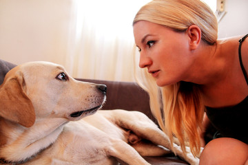 Woman with dogs. The dog gives a paw her female owner on sofa. Happy Pretty girl petting and looking her Yellow labrador retriever dog laying in the bed at home. Owner having fun with his pet concept.