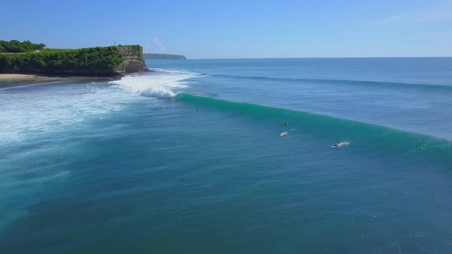 AERIAL: Surfing fail and slam - unrecognizable surfer falling off the board when riding big foamy whitewater wave in sunny Bali. Waterdrops splashing and spraying around creating rainbow. Wipe out