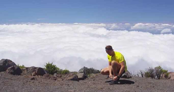 Runner athlete tying shoelaces going running on mountain above clouds. Young man is preparing to workout in nature on sunny day. RED EPIC SLOW MOTION.