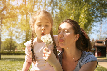 Mother and daughter blowing dandelion. Single mother enjoying with her little daughter in the...