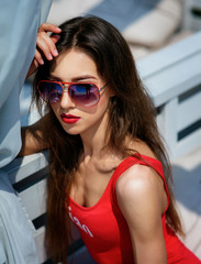 Pretty woman in red swimsuit sits on white sofa outside