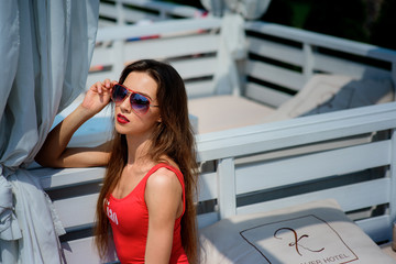 Pretty woman in red swimsuit sits on white sofa outside