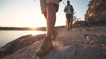 Anonymous group of multiethnic people with backpacks walking on rocky shore in sunlight while hiking.