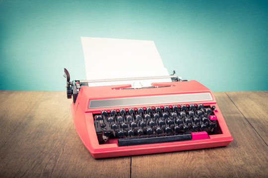 Retro old typewriter from 70s with paper blank on wooden table. Vintage style filtered photo