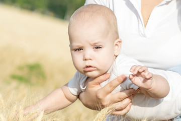 Portrait of a adorable newborn baby on his mother's arms outdoor in wheat field at sunny summer day