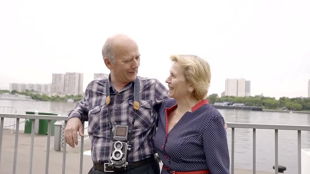 older couple of retirement age are by the river in a big city. fun with smiles talking. a happy old age