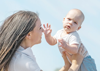Portrait of a small newborn baby boy and his mother throwing him up to blue sky iat sunny summer day