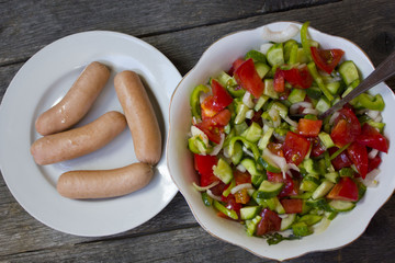 sausages , salad of cucumber, tomato, pepper on a wooden table