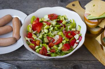 sausages , salad of cucumber, tomato, pepper on a wooden table