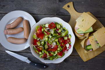 sausages , salad of cucumber, tomato, pepper on a wooden table