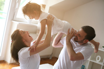 Happy family with one daughter spending time at home.  Parents playing with their daughter on bed.