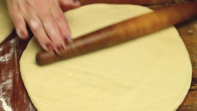 Process of making pie, woman's hands with rolling pin roll the dough on wooden table, close-up