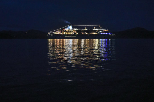 A cruise ship sailing down the Norwegian coast at night, shining with lights.