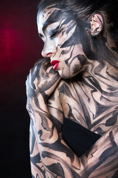 A painted woman embraces herself with black paint.