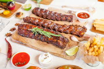 Spicy hot grilled spare ribs from a summer BBQ served with chips, corn and fresh tomatoes on an old wooden cutting board