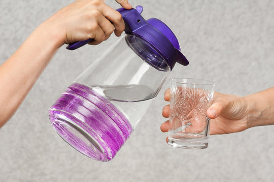 hands pouring water from a jug into a glass