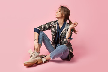 Beautiful smiling woman on a pink background  in a military jacket with camouflage pattern  in jeans and  rough shoes