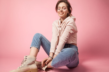 Stylish young woman sitting on a pink background in jeans  and in rough shoes