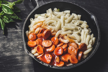 Pasta with sausages, tomato sauce and basil in a cast-iron frying pan on a tenor background