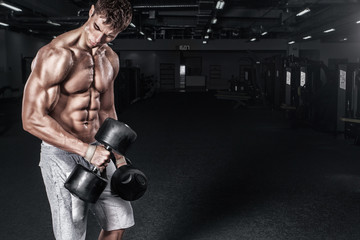 Athletic shirtless young sports man - fitness model holds the dumbbell in gym. Copy space fore your...