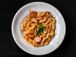 Pasta with sausages, tomato sauce and basil in a white plate on a tenor background