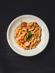 Pasta with sausages, tomato sauce and basil in a white plate on a tenor background
