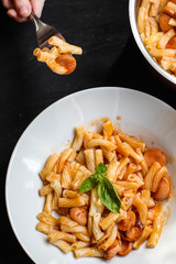 Pasta with sausages, tomato sauce and basil in a white plate on a tenor background