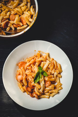 Pasta with sausages, tomato sauce and basil in a white plate on a tenor background