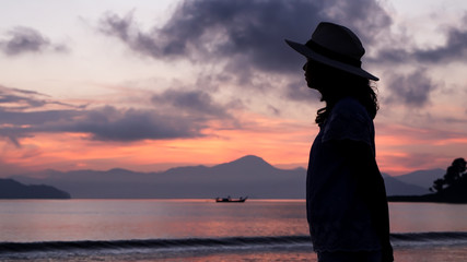 Fototapeta premium Asian woman silhouette at sunrise ocean pink and orange sky