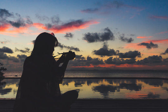 Silhouette of a woman taking the picture of sunset on the swimming pool near the beach.