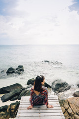 Rear view of woman sitting on the bridge and looking to sea.