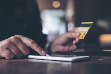 Closeup image of a woman's hand holding credit card and pressing at mobile phone on wooden table in office